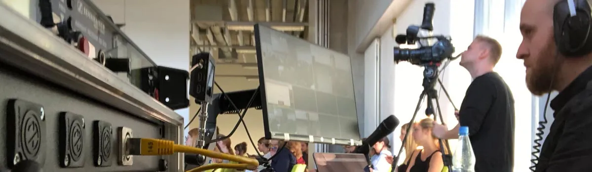 Teilnehmer mit Kopfhörern und Kamera vor einem Monitor im Studio